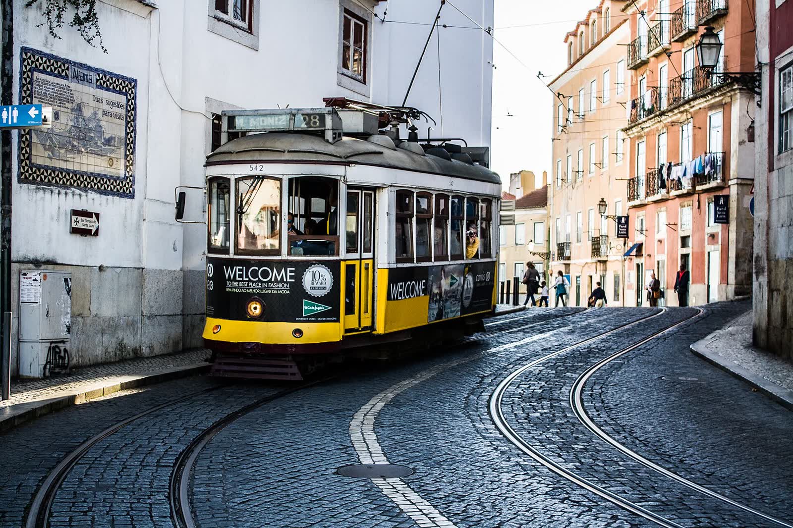 A yellow Tram 28 rounding a cobbled bend in Lisbon's Alfama district