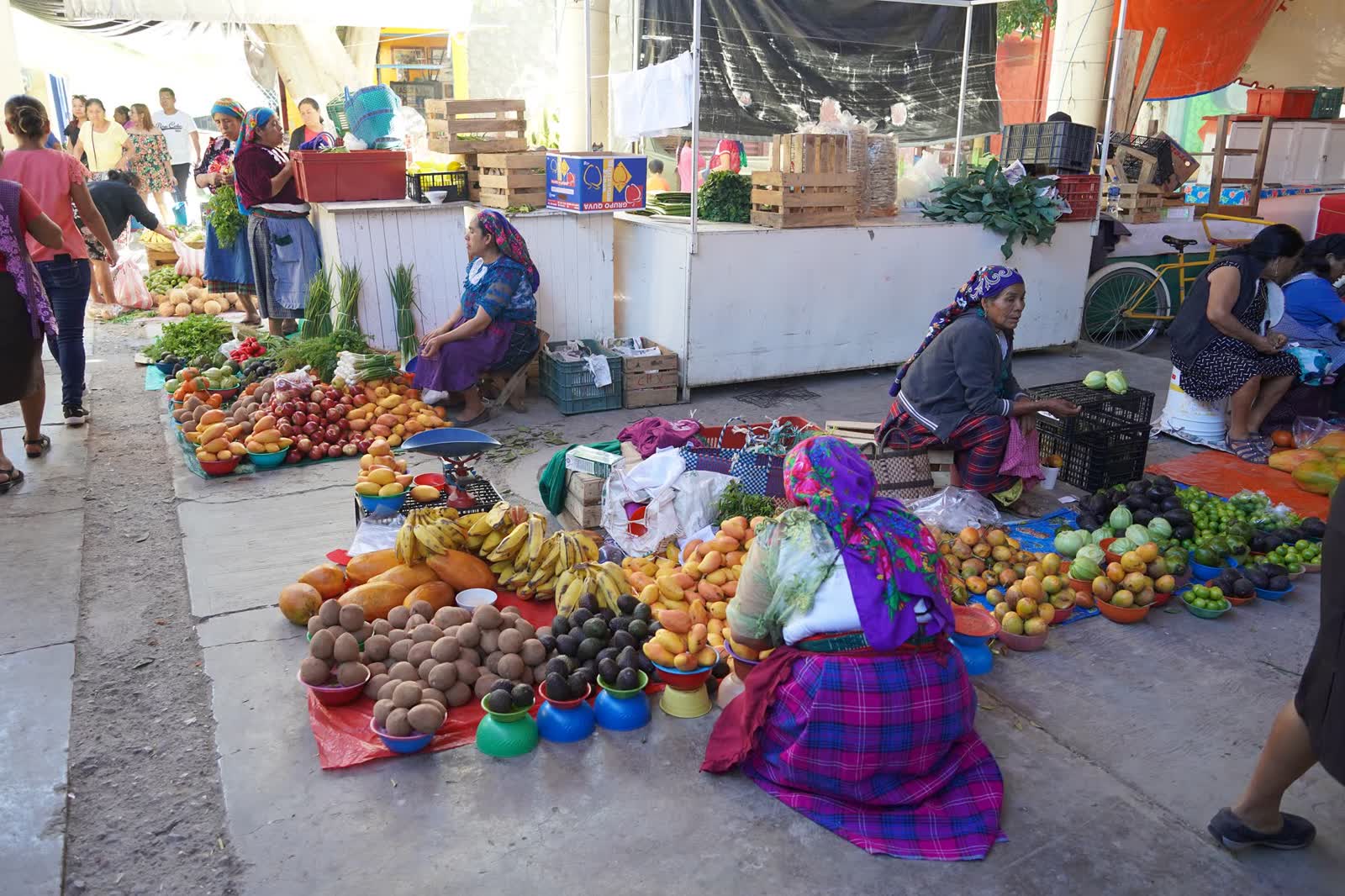 Market stalls piled with fruit and vegetables in Oaxaca, with vendors seated on the ground